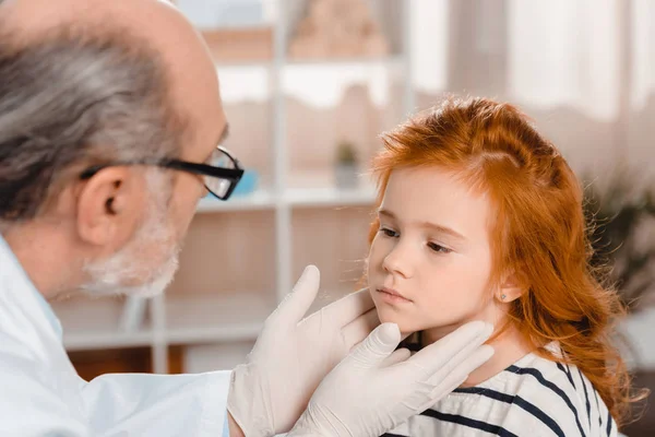 Pediatra senior en guantes médicos examinando a pequeños pacientes garganta en la clínica — Stock Photo