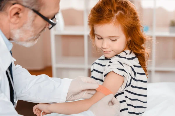 Médico senior poniendo yeso en el brazo de los pacientes después de la inyección en la clínica - foto de stock