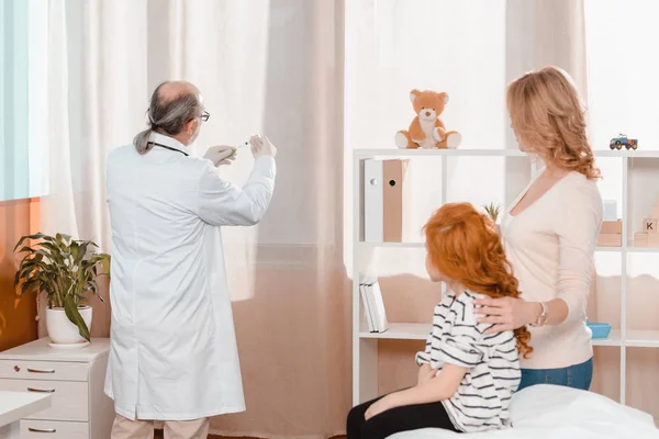 Doctor in medical gloves with syringe going to make injection to little girl in clinic — Stock Photo