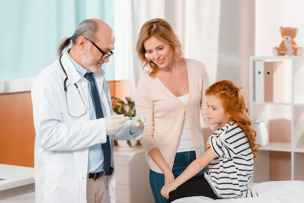 Doctor in medical gloves with syringe going to make injection to little girl in clinic — Stock Photo