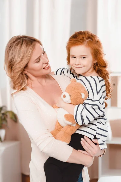 Retrato de mãe sorridente segurando pequena filha com ursinho de pelúcia — Fotografia de Stock