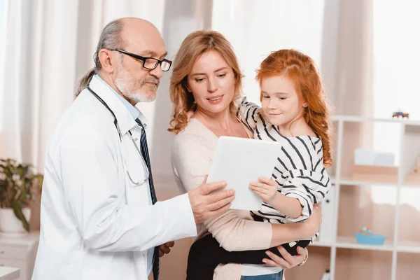 Retrato de médico de casaco branco, mulher e filha usando tablet juntos na clínica — Fotografia de Stock