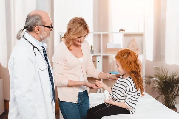 Side view of little girl giving pills to mother during doctors reception in clinic — Stock Photo