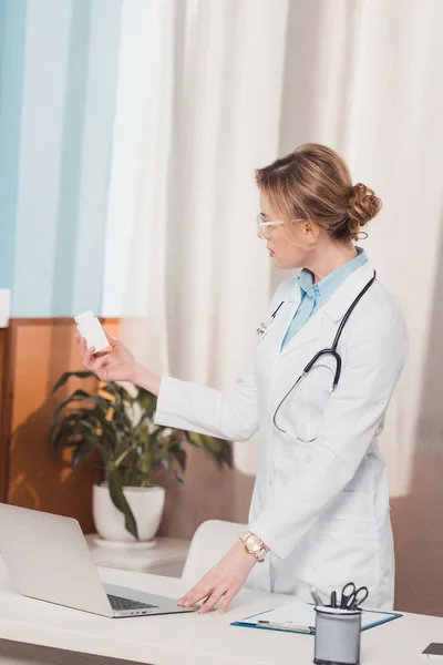 Retrato del médico de bata blanca con medicamentos en la mano de pie en el lugar de trabajo en la clínica - foto de stock