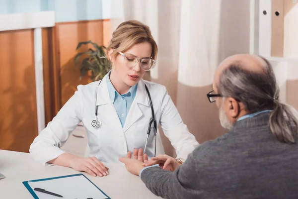 Focalizzazione selettiva del medico femminile concentrato negli occhiali che controlla il polso dei pazienti in clinica — Foto stock