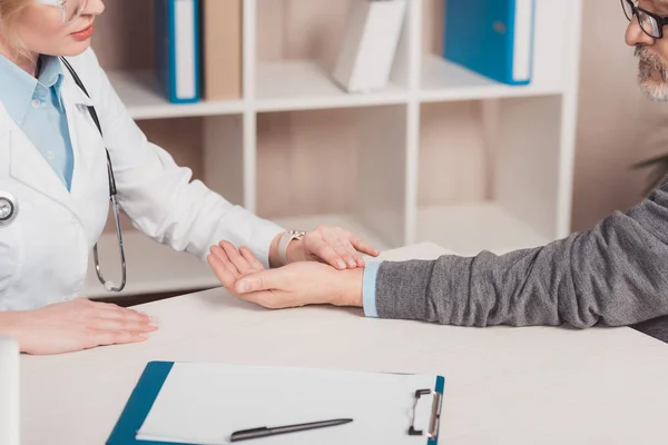 Vista parziale del medico donna che controlla il polso dei pazienti in clinica — Foto stock