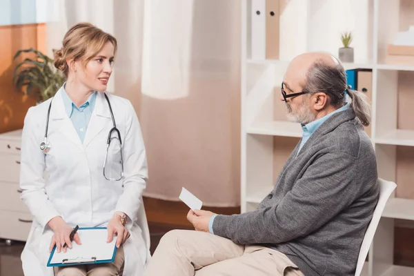 Arzt im weißen Kittel mit Notizblock hört Patienten in Klinik zu — Stockfoto