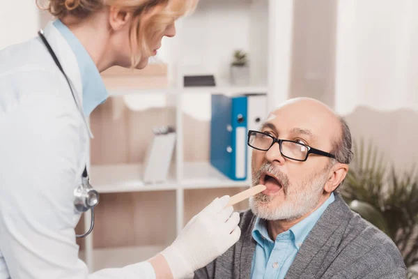 Selective focus of doctor in medical gloves checking patients throat in clinic — Stock Photo