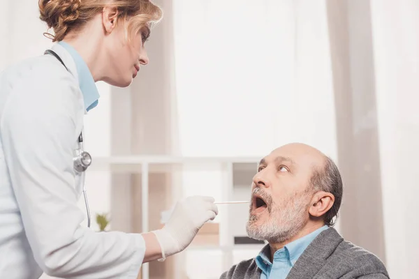 Side view of doctor in medical gloves checking patients throat in clinic — Stock Photo