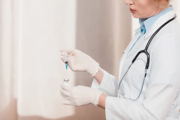 Partial view of doctor in white coat and medical gloves holding syringe for injection in hands in clinic — Stock Photo
