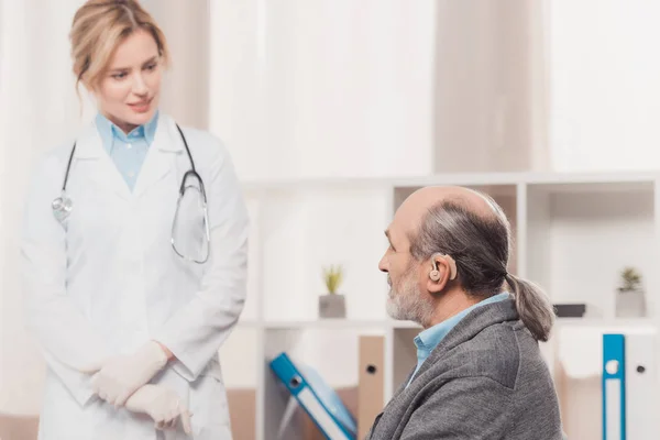 Selective focus of senior patient with deaf-aid at doctors reception in clinic — Stock Photo