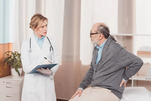 Doctor in white coat with notepad listening to patients complaint in clinic — Stock Photo