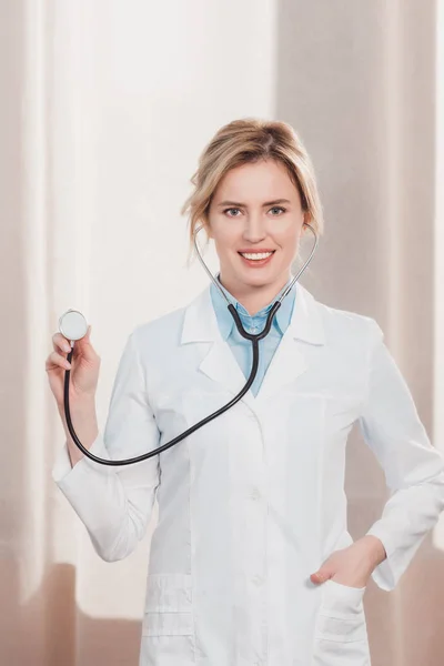 Портрет усміхненої жінки-лікаря в білому пальто, що показує стетоскоп в руці — стокове фото