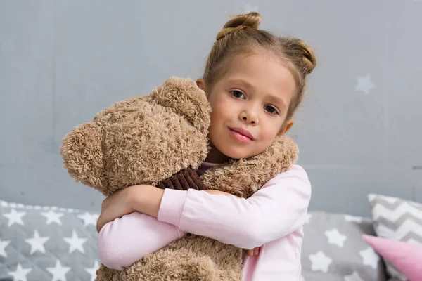 Entzückendes kleines Kind umarmt ihren Teddybär und blickt in die Kamera — Stockfoto