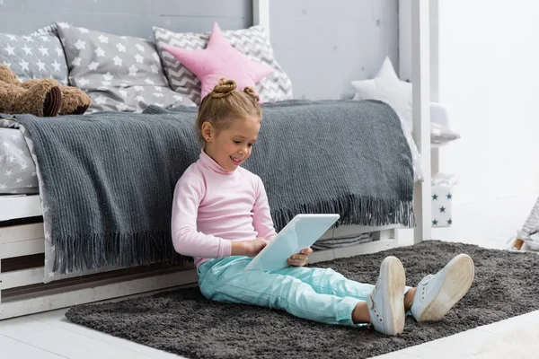 Criança sorrindo sentada no chão e usando tablet — Fotografia de Stock