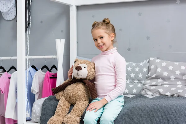 Happy little kid sitting in bed with teddy bear — Stock Photo