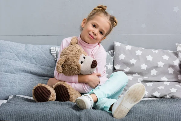 Smiling little kid sitting in bed with teddy bear — Stock Photo