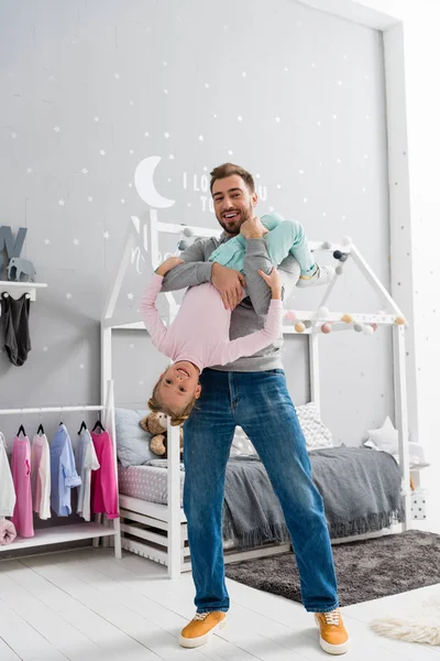 Feliz padre joven jugando con la hija en el dormitorio del niño - foto de stock