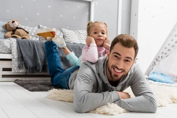 Feliz joven padre e hija tumbados en el suelo en el dormitorio de los niños - foto de stock
