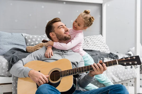 Padre feliz tocando la guitarra para la hija en el piso del dormitorio del niño - foto de stock