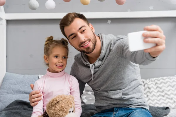 Bello giovane padre e figlia con orsacchiotto prendere selfie — Foto stock