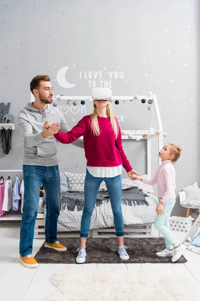 Jeune famille heureuse utilisant casque de réalité virtuelle dans la chambre des enfants — Photo de stock