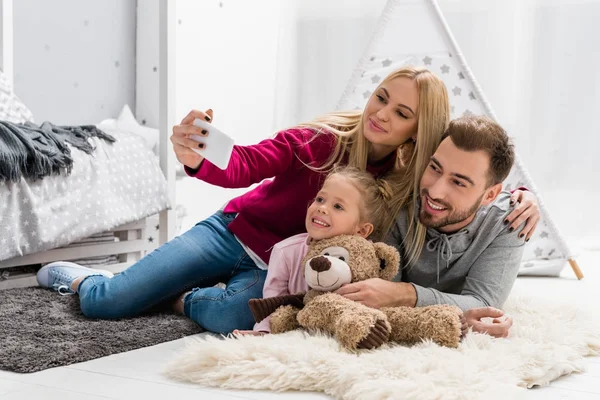 Felice giovane famiglia prendendo selfie mentre sdraiati sul pavimento insieme — Foto stock