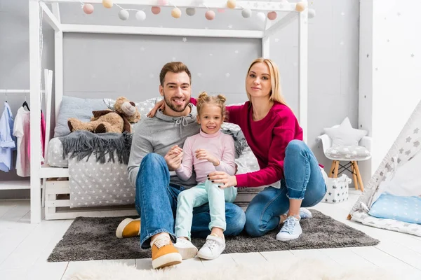 Happy young family sitting on floor of kid bedroom together — Stock Photo