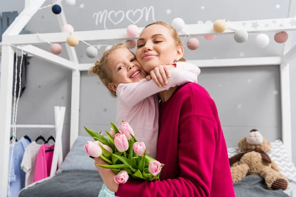 Tochter überreicht Tulpenstrauß für Mutter am Muttertag und umarmt sie — Stockfoto