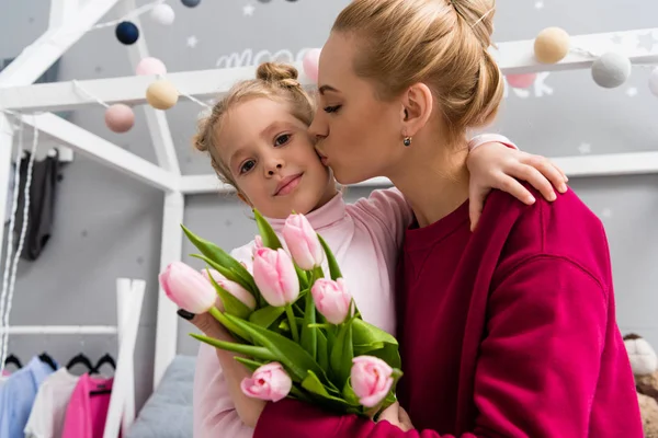 Beautiful young mother with tulips bouquet kissing daughter — Stock Photo