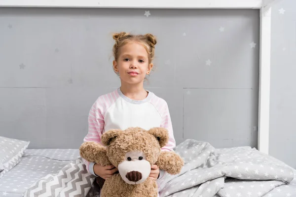 Adorable little kid with teddy bear sitting on bed — Stock Photo