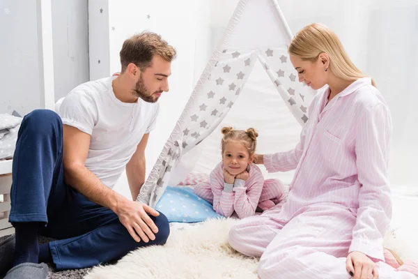 Adorable little daughter spending time with parents while relaxing in handcrafted teepee on floor — Stock Photo