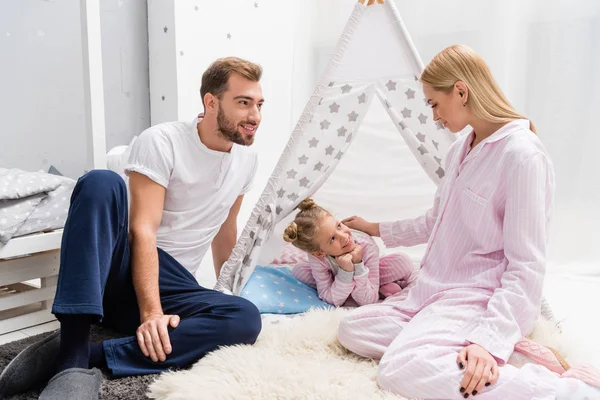 Little daughter spending time with parents while sitting in handcrafted teepee on floor — Stock Photo
