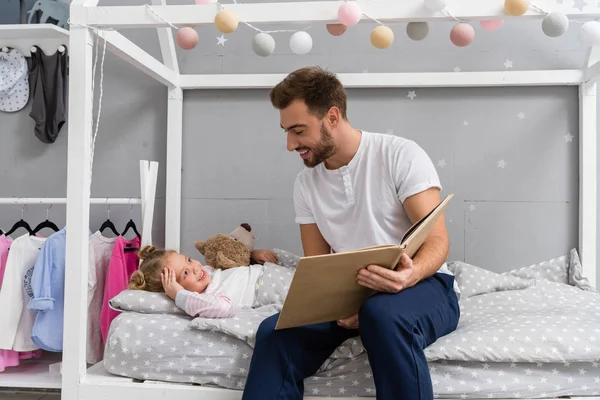 Feliz jovem pai ler livro para a filha na cama — Fotografia de Stock