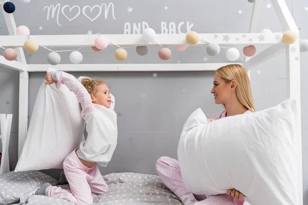 Happy mother and daughter in pajamas fighting with pillows — Stock Photo