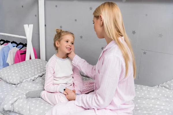 Feliz madre e hija sentadas en la cama en el dormitorio de los niños - foto de stock