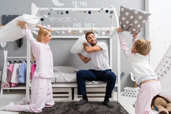 Красивая молодая семья дерется с подушками в детской спальне — стоковое фото