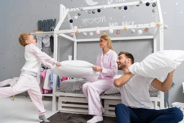 Смеющаяся молодая семья, дерущаяся с подушками в детской спальне — стоковое фото