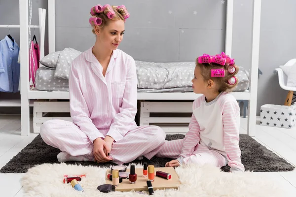 Mother and daughter in pajamas with hair rollers on head sitting on floor — Stock Photo