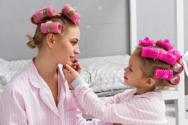Прелестная дочь делает макияж нанося помаду на губы матери — стоковое фото