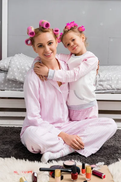 Happy mother and daughter with hair rollers and in pajamas sitting on floor — Stock Photo