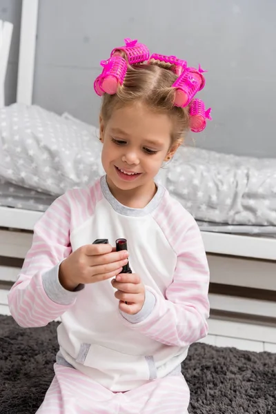 Adorable little kid with hair rollers on head opening bottle with nail polish — Stock Photo