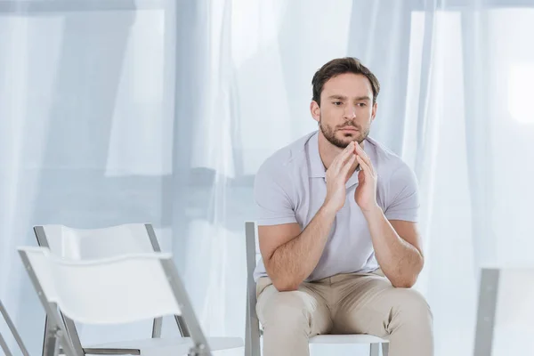 Депрессивный мужчина средних лет сидит на стуле и смотрит в пустую комнату — стоковое фото