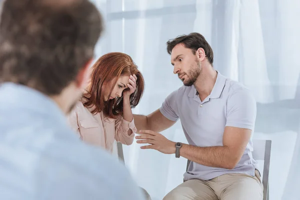 Selective focus of man supporting upset middle aged woman during group therapy — Stock Photo