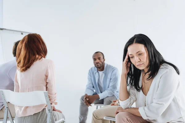 Depressed asian woman looking down and multiethnic group sitting behind — Stock Photo