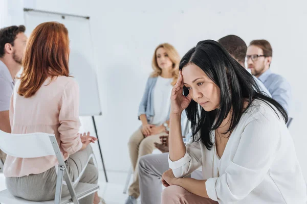 Close-up view of upset asian middle aged woman and people sitting on chairs behind during group therapy — Stock Photo