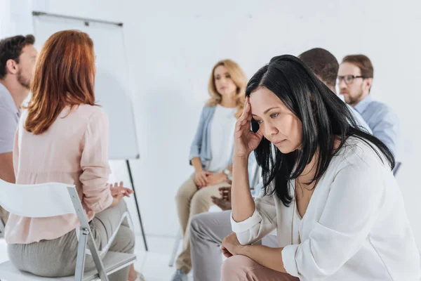 Nahaufnahme einer aufgebrachten asiatischen Frau mittleren Alters und Menschen, die während einer Gruppentherapie auf Stühlen hinter ihr sitzen — Stockfoto