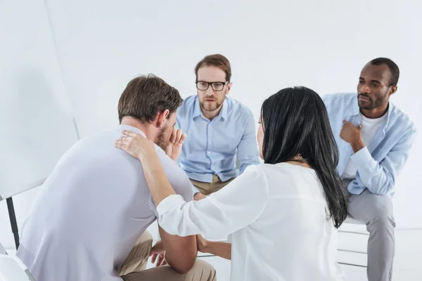 Personnes adultes moyennes multiethniques assises sur des chaises et soutenant l'homme bouleversé pendant la thérapie de groupe anonyme — Photo de stock