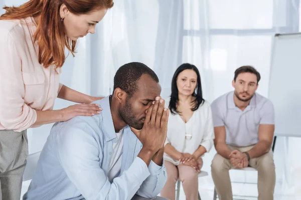 Personnes d'âge moyen soutenant l'homme afro-américain contrarié pendant la thérapie de groupe anonyme — Photo de stock