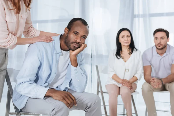 Abgeschnittene Haut von Menschen mittleren Alters, die einen depressiven afrikanisch-amerikanischen Mann während einer anonymen Gruppentherapie unterstützen — Stockfoto